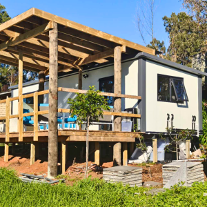 Side view of a 9.91m x 3m portable cabin with a timber deck and covered patio