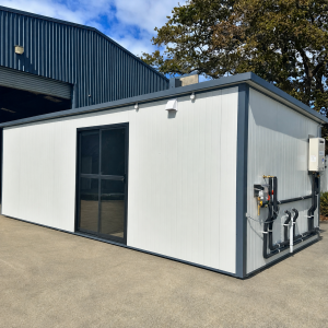 Angled view of an 8.08m x 3m portable cabin with a glazed entrance and exterior plumbing